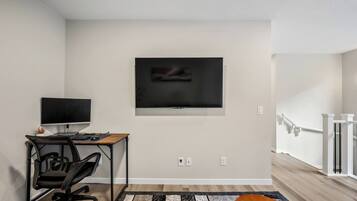 A modern living room with a flat-screen TV mounted on the wall, a desk with a computer, and a chair.