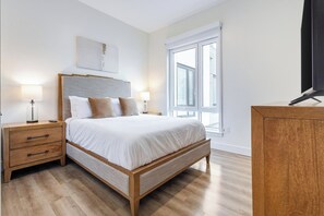 A bedroom with a bed, bedside tables, a nightstand, a window, and a television. - Landing | Modern 1BD, Pool (West Hartford)