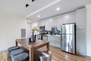 Een moderne keuken met een roestvrijstalen koelkast, een houten eettafel met vier stoelen, en een vaas met planten.