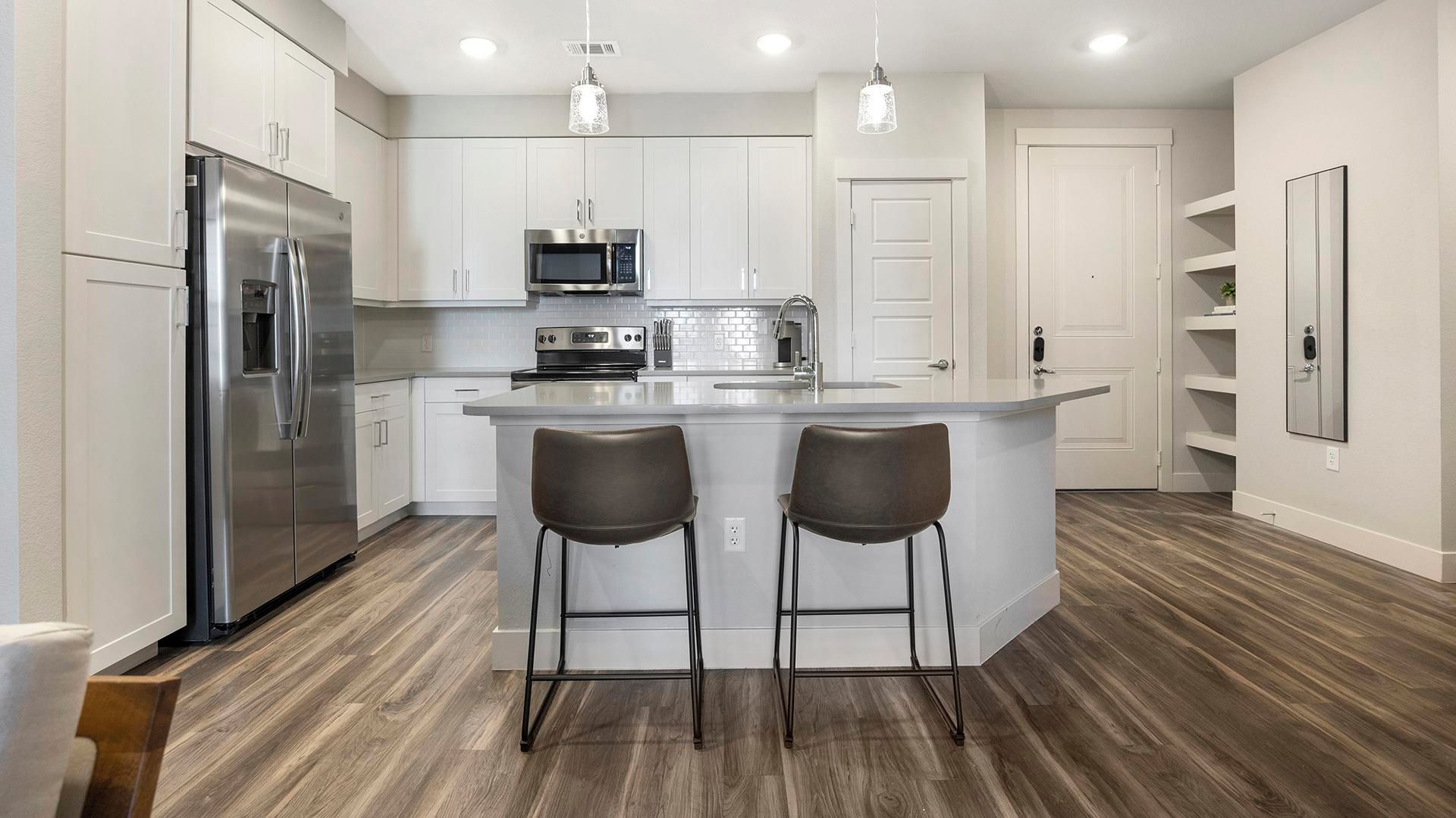 A modern kitchen with a stainless steel refrigerator, a microwave, and a stove. There are two bar stools at the island.