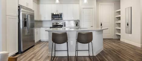 A modern kitchen with a stainless steel refrigerator, a microwave, and a stove. There are two bar stools at the island.