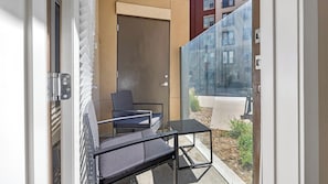 Ein Balkon mit Stuhl und kleinem Tisch, einer Schiebetür und Blick auf die Straße und die Häuser.