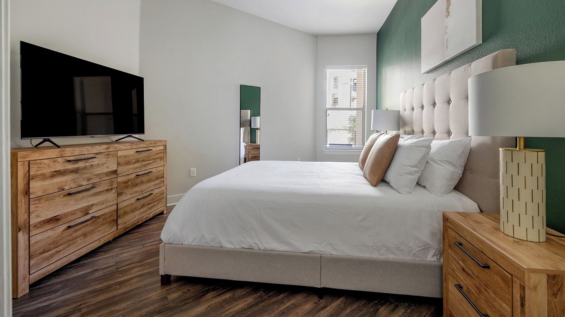 Een slaapkamer met een bed, een houten dressoir, een televisie en een raam.