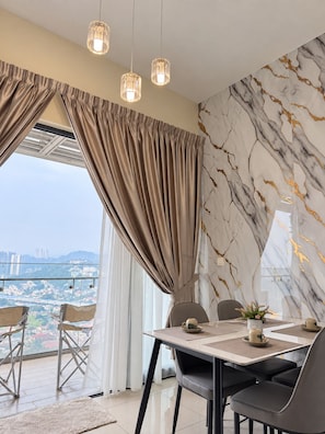 Ein moderner Essbereich mit einem Tisch für zwei Personen, Blick auf die Stadt durch große Fenster und einer Wand mit Marmormuster.