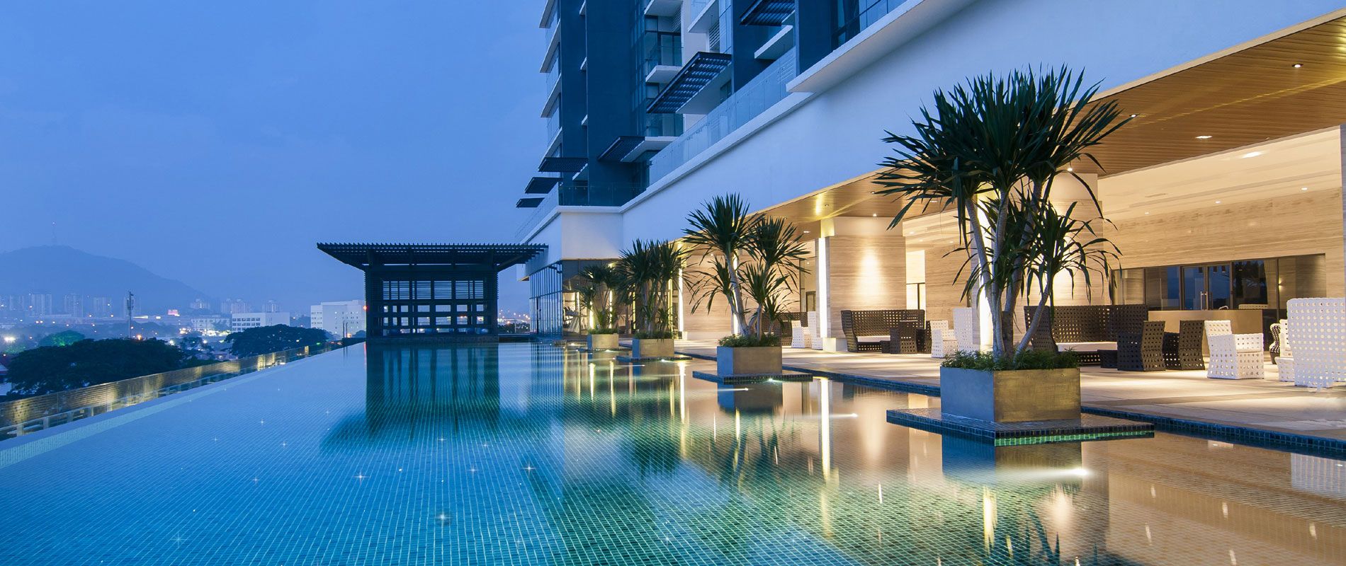 Ein Pool ohne Rand auf dem Dach mit Blick auf eine Stadtlandschaft, ein modernes Gebäude mit Holzfassade und eine traditionelle Pavillonarchitektur.