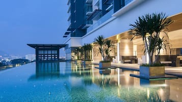 Ein Pool ohne Rand auf dem Dach mit Blick auf eine Stadtlandschaft, ein modernes Gebäude mit Holzfassade und eine traditionelle Pavillonarchitektur.