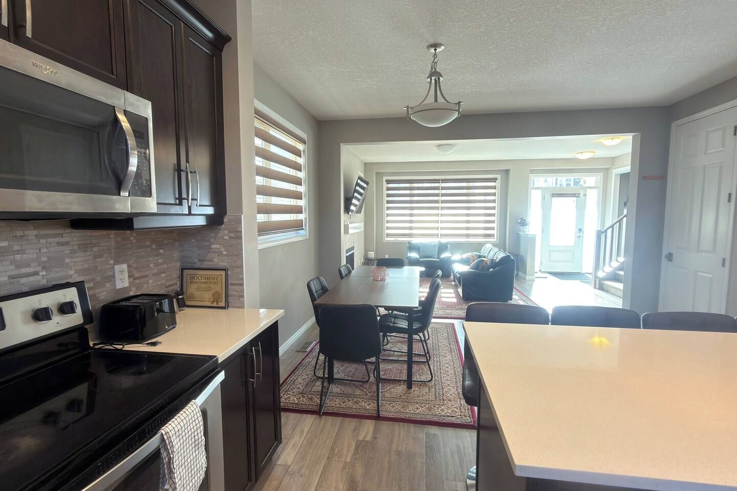 A modern kitchen with a central island, dining area with chairs, and a view to the living room.