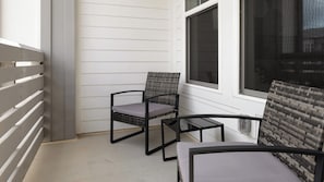 Ein Balkon mit zwei Stühlen und einem kleinen Tisch, weißen Wänden und einem Fenster.