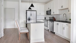Eine moderne Küche mit weißen Schränken, einem Edelstahl-Kühlschrank, einer Mikrowelle und einer Kaffeemaschine.