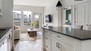 A modern kitchen with white cabinetry, a black countertop, and a flat-screen TV mounted above the sink. - Landing | Stylish 1BD, Game Room, Gym (Gainesville)