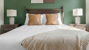 A neatly made bed with a white duvet and two brown pillows, flanked by two bedside tables with lamps. - Landing | Stylish 1BD, Pool, Game Room (Gainesville)