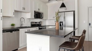 A modern kitchen with white cabinetry, stainless steel appliances, a central island, and a pendant light. - Landing | Stylish 1BD, Pool, Game Room (Gainesville)