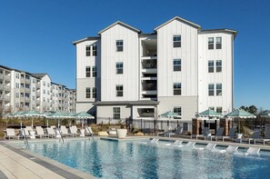 A multi-story hotel with a swimming pool, outdoor seating, and a clear blue sky. - Landing | Stylish 1BD, Pool, Game Room (Gainesville)