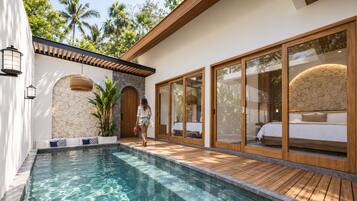 A pool area with a wooden deck, a stone wall, and a glass-enclosed bedroom with a bed.