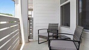 A balcony with white siding, two wicker chairs with cushions, and a window with a screen. - Landing | Chic 1BD, Game Room, Pool (Gainesville)