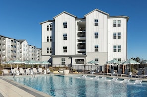 A multi-story hotel with a swimming pool, outdoor seating, and a clear blue sky. - Landing | Chic 1BD, Pool, Gym (Gainesville)