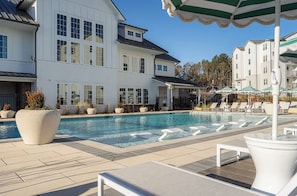A swimming pool with lounge chairs and umbrellas, surrounded by white buildings with large windows. - Landing | Beautiful 2BD, Game Room, Pool (Gainesville)