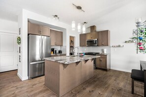 Une cuisine moderne dotée d’un îlot central, d’appareils électroménagers en acier inoxydable et de meubles de rangement en bois.
