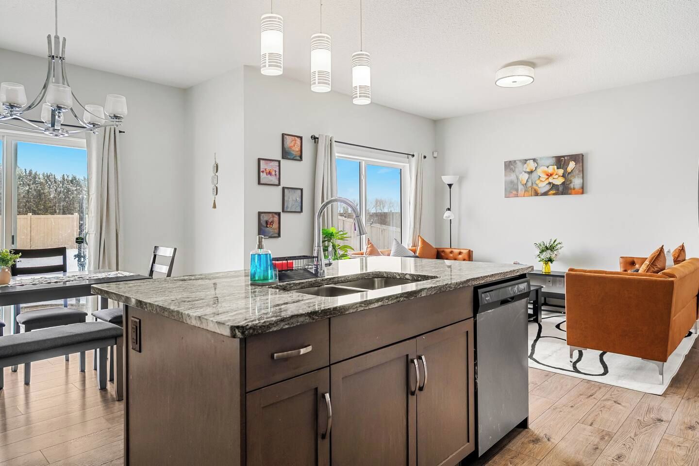 Cozinha moderna com ilha central, área de refeições com banco e sala de estar com sofá e mesa de centro.