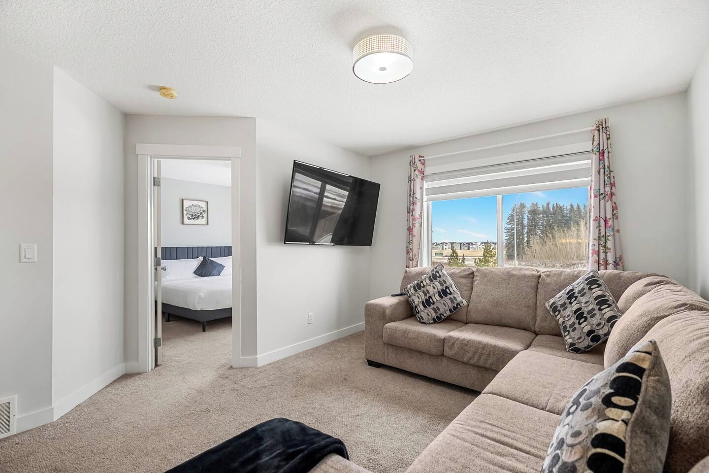 A living room with a sofa, a television, a bed in the adjacent room, and a window with a view.
