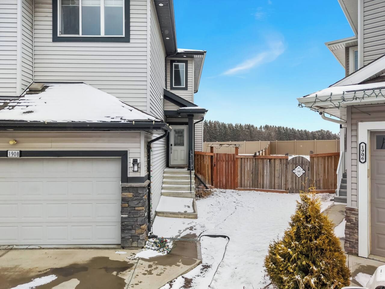 A residential property with a garage, a wooden fence, and a snow-covered driveway.
