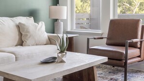 A living room with a sofa, a chair, a coffee table, a lamp, and a plant. - Landing | Beautiful 2BD, Game Room, Gym (Gainesville)