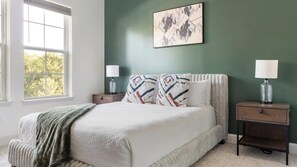 A bedroom with a bed, two bedside tables, a window, and a wall-mounted artwork. - Landing | Beautiful 2BD, Game Room, Gym (Gainesville)