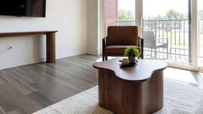 A modern living room with a wooden coffee table, a brown leather chair, and a television mounted on the wall. - Landing | Amazing 1BD, Gym (Council Bluffs)