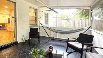Een overdekt terras met een hangmat, zitplaatsen en een tafeltje met een plant.