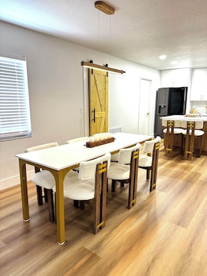 A modern kitchen with a wooden table and chairs, a sliding barn door, and a black refrigerator.
