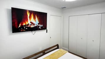 Un dormitorio con una cama, un televisor mostrando una chimenea y un armario.