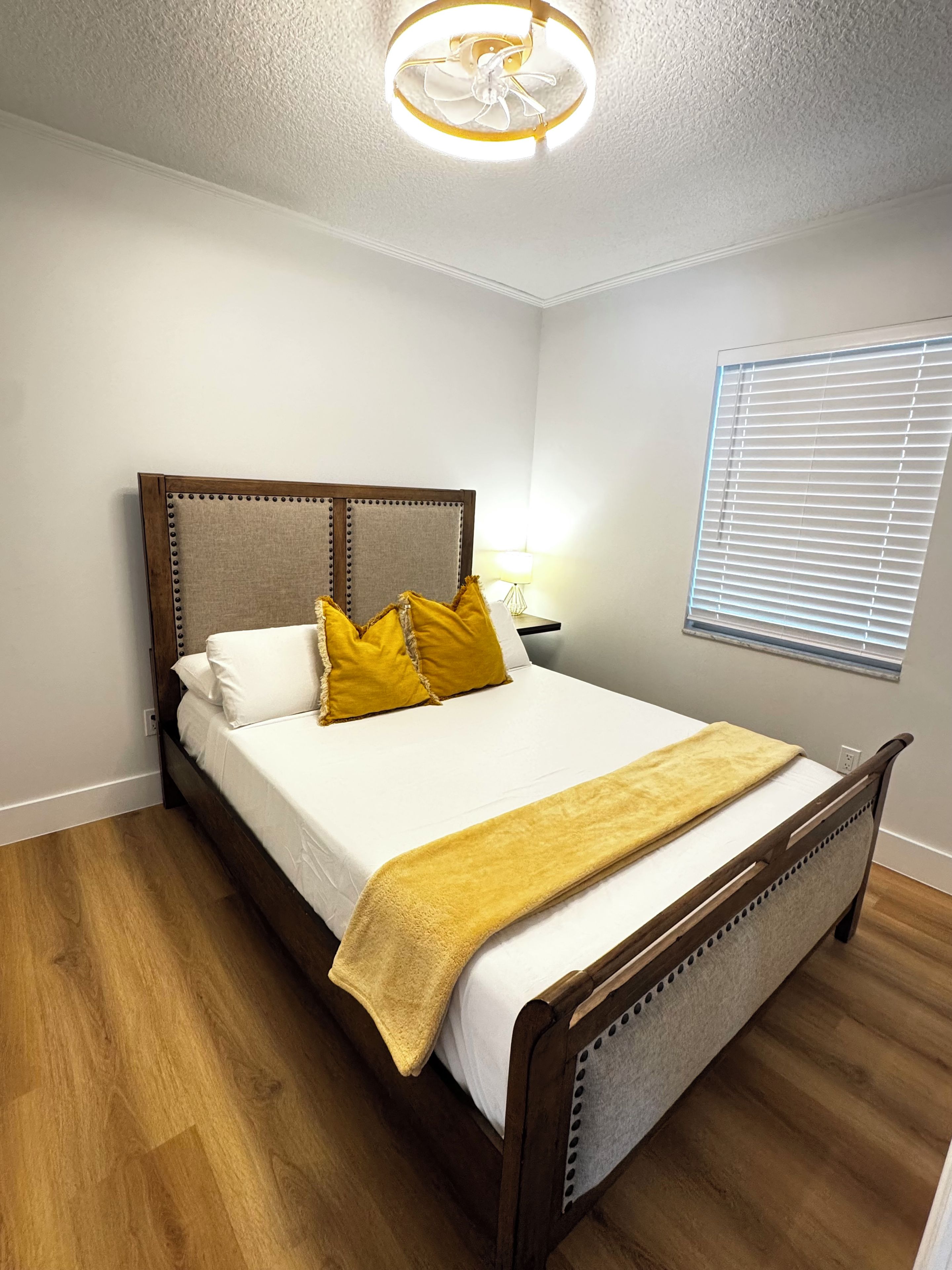 Een slaapkamer met een houten bed, witte beddengoed en een gele plaid.