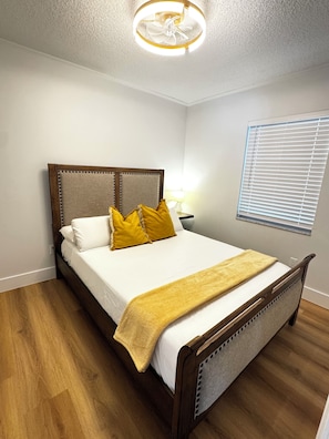 Een slaapkamer met een houten bed, witte beddengoed en een gele plaid.