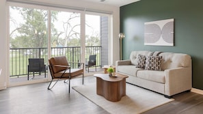 A living room with a sofa, a chair, a coffee table, and a view through a sliding glass door to the outdoors.