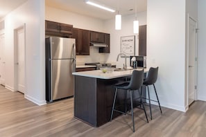 A modern kitchen with stainless steel appliances, a central island with bar stools, and a 'GYM NOW' motivational poster.
