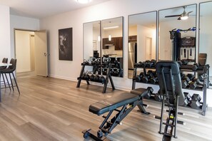Ein Fitnessraum mit Trainingsgeräten, einer Bank, Kettlebells und Kurzhanteln.