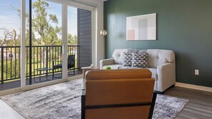 A living room with a sofa, a coffee table, and a view of a deck. - Landing | Chic 2BD, Gym (Council Bluffs)