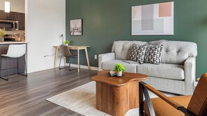 Een moderne woonkamer met een grijze bank, een houten salontafel en een eethoek met een witte stoel en een kleine tafel.