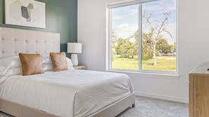 A bedroom with a large window, a bed with white bedding, a headboard, and a nightstand with a lamp. - Landing | Beautiful 1BD, Gym (Council Bluffs)