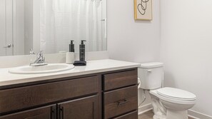 A bathroom with a white sink, dark wooden vanity, a mirror, a toilet, and a framed artwork on the wall. - Landing | Beautiful 1BD, Gym (Council Bluffs)