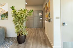 A hallway with a potted plant, a door with a 'Mechanical' sign, and a 'Parcel Pending' sign on a grey cabinet. - Landing | Incredible 1BD, Gym (Council Bluffs)