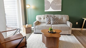 A living room with a sofa, a coffee table, a lamp, and a painting on the wall. - Landing | Incredible 1BD, Gym (Council Bluffs)
