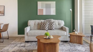 A living room with a sofa, two wooden side tables, a small plant, and a framed picture on the wall. - Landing | Modern 2BD, Gym (Council Bluffs)
