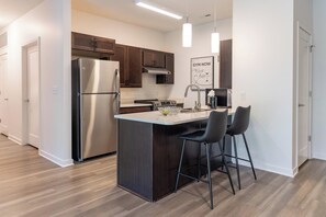 A modern kitchen with stainless steel appliances, a central island with bar stools, and a 'GYM NOW' motivational poster. - Landing | Incredible 1BD, Gym (Council Bluffs)