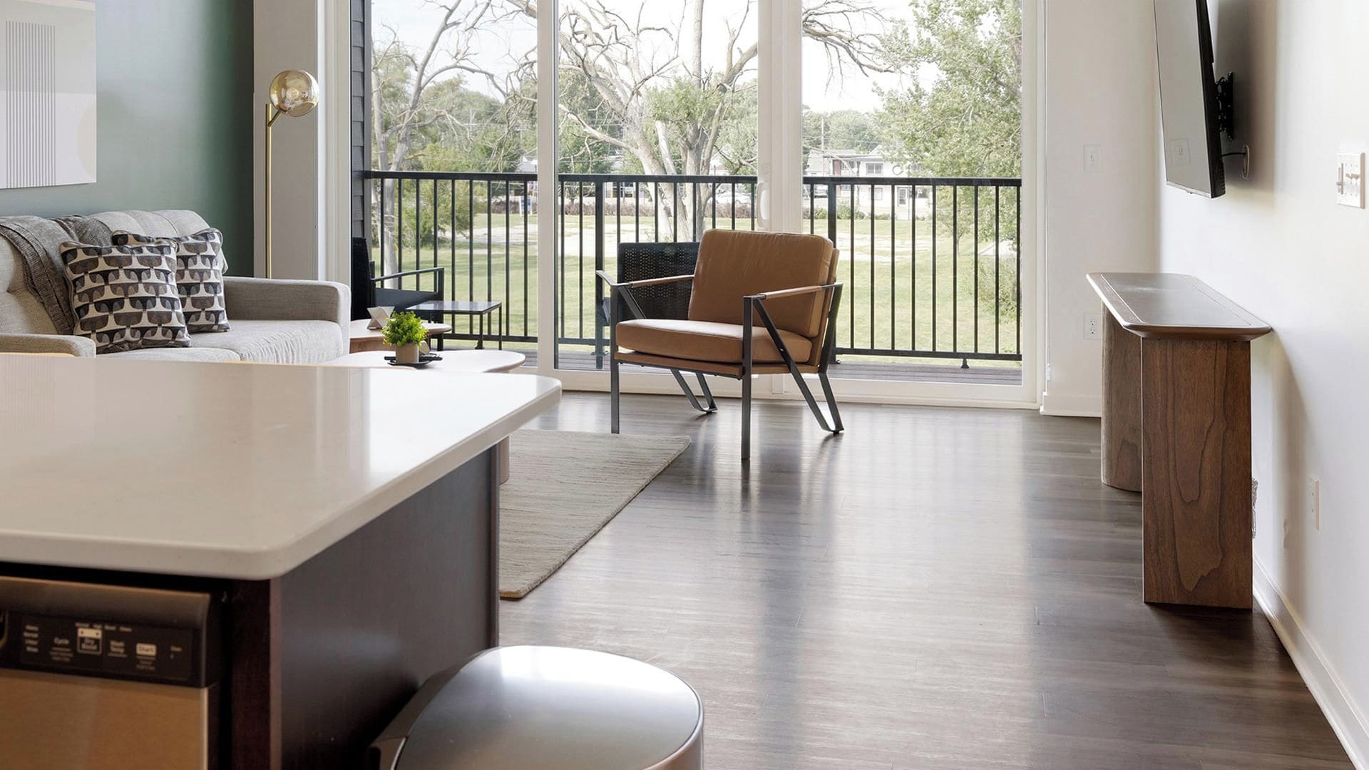 A modern kitchen with a built-in dishwasher, a dining area with a table and chairs, and a view of a backyard through a glass door.