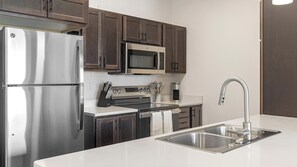 A modern kitchen with stainless steel appliances, a double sink, and wooden cabinets. - Landing | Chic 1BD, Gym (Council Bluffs)