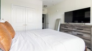 Une chambre à coucher avec un lit, une commode, un téléviseur et une porte.