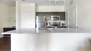 A modern kitchen with a large island, stainless steel appliances, and a dark wood floor. - Landing | Stunning 1BD, Gym, Clubhouse (Jacksonville)