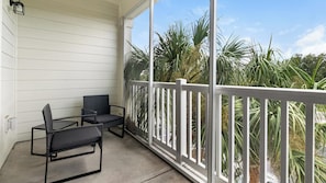 A balcony with two chairs and a table, white railings, and a view of palm trees. - Landing | Stunning 1BD, Gym, Clubhouse (Jacksonville)