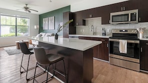 A modern kitchen with a central island, bar stools, stainless steel appliances, and a view to the left. - Landing | Stylish 1BD, Gym, Clubhouse (Jacksonville)